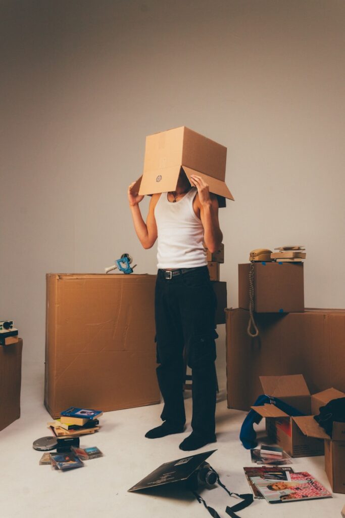 Man wearing a box surrounded by moving supplies.